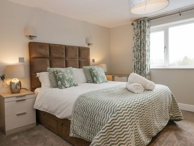 A bedroom with a bed with green patterned pillows and blanket bedside tables and window at Holme Fell in Coniston