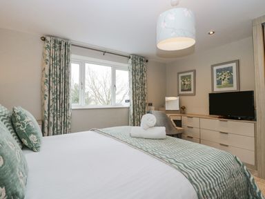 A bedroom with a bed pillows and folded towels a window curtains a dresser with a TV and chair at Holme Fell in Coniston