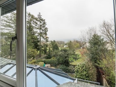 A view of trees and greenery through a window with a glass roof below at Holme Fell in Coniston