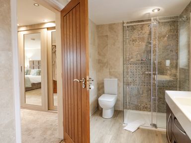 A bathroom with a toilet shower with glass doors and a sink visible through an open wooden door with a bedroom and mirrored wardrobe visible in the background at Holme Fell Coniston