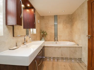 A bathroom with a white sink and wooden cabinets next to a bathtub with tiled walls at Holme Fell in Coniston