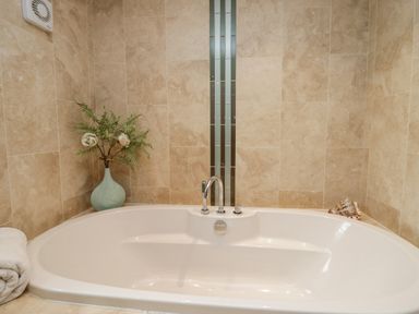 A bathtub with a faucet surrounded by beige tiled walls with a vase of flowers and a rolled towel at Holme Fell in Coniston