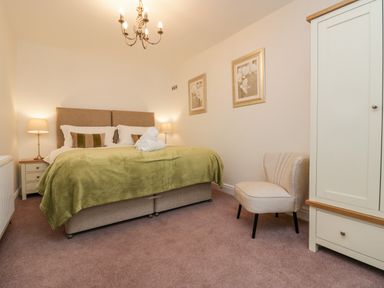 A bedroom with a double bed green blanket bedside tables lamps an armchair and a wardrobe at Holme Fell in Coniston