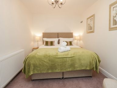 A bedroom with a bed with green blanket and two rolled towels with bedside lamps and framed pictures on the wall at Holme Fell in Coniston
