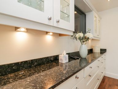 A kitchen counter with a tissue box remote controls a vase with white flowers and a bread container at Holme Fell in Coniston