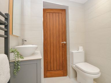 A bathroom with a white toilet and sink a wooden door and light-colored tiles at Holme Fell in Coniston