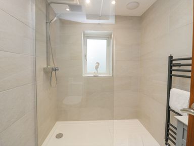 A shower area with a glass screen a wall-mounted shower head a small window and a towel rack in a bathroom at Holme Fell in Coniston