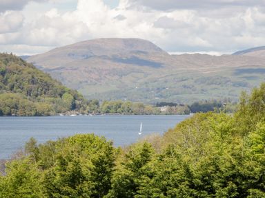 A lake with a sailboat surrounded by trees and hills in the background at Holme Fell in Coniston