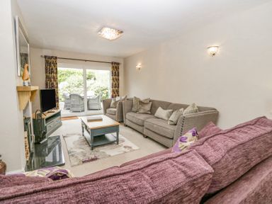A living room with sofas a coffee table television and sliding glass doors leading to a patio at Holme Fell in Coniston