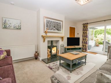 A living room with a wood stove fireplace a television on a stand a coffee table and sliding glass doors leading outside at Holme Fell in Coniston