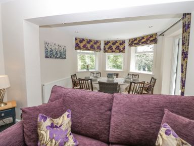 A dining area with a table set for six and purple floral curtains behind a purple sofa at Holme Fell in Coniston