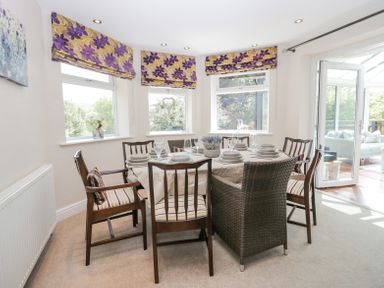 A dining room with a table set with plates and glasses surrounded by chairs and windows with floral blinds at Holme Fell in Coniston