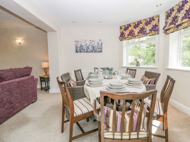 A dining table set with bowls and glasses surrounded by wooden and wicker chairs in a room with patterned purple and yellow window blinds at Holme Fell in Coniston
