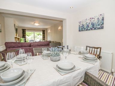 A dining table set with plates bowls and wine glasses in a room with sofas and a sliding glass door at Holme Fell in Coniston