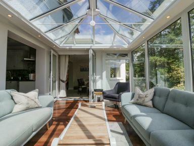 A sunroom with two light blue sofas a wooden coffee table and glass walls at Holme Fell in Coniston