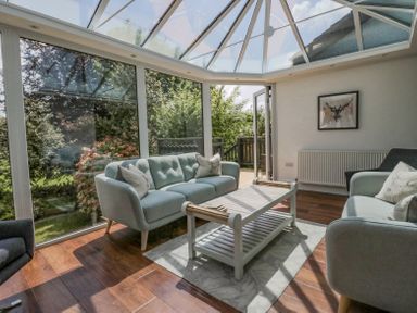 A conservatory with sofas a coffee table wooden floor and glass ceiling at Holme Fell in Coniston