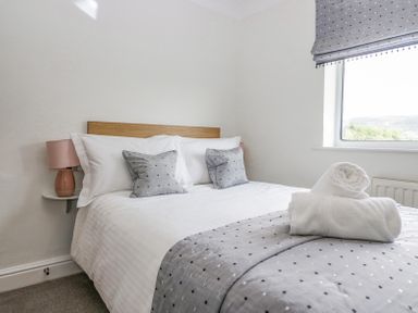 A bedroom with a made bed two pillows two cushions bedside lamp and window at Holme Fell in Coniston