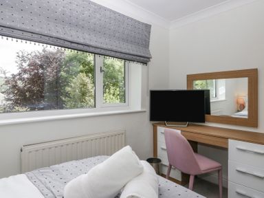 A bedroom with a window, desk with a mirror, television, and a pink chair at Holme Fell in Coniston