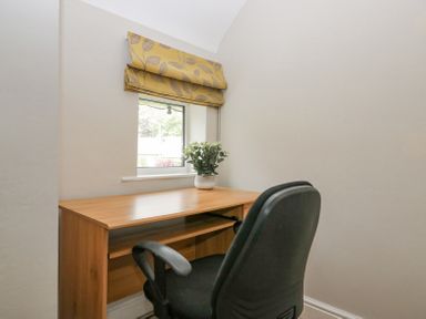 A small workspace with a wooden desk a black office chair a plant on the desk and a window with a yellow patterned blind at Holme Fell in Coniston