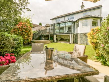A garden with a glass table and chairs with a champagne bucket and glasses outside a house with a conservatory at Holme Fell in Coniston