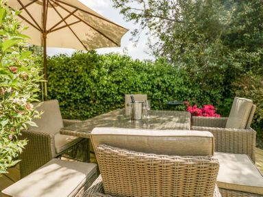 An outdoor patio with a wicker dining table and chairs under a large umbrella with plants around at Holme Fell in Coniston