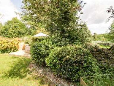 A garden with shrubs trees and a patio area with chairs and an umbrella at Holme Fell in Coniston