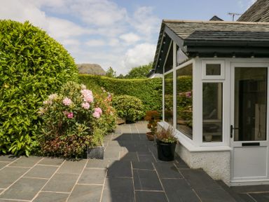 A garden patio area with potted plants and bushes next to a house with large windows at Holme Fell in Coniston