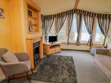 A living room with a fireplace a rocking chair a TV on a wooden cabinet a sofa and striped curtains at Rosehaven in Tegryn near Crymych