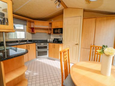 A kitchen with wooden cabinets a stove a microwave a round dining table with chairs and a vase with flowers at Rosehaven in Tegryn near Crymych