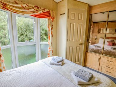 A bedroom with a bed covered in towels next to a window with curtains and a mirrored wardrobe at Rosehaven in Tegryn near Crymych