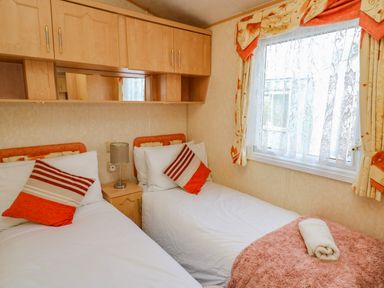 A bedroom with two single beds white bedding bedside table with lamp window with curtains and overhead cabinets at Rosehaven in Tegryn near Crymych