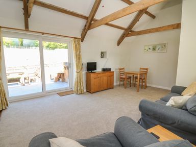 A living room with wooden beams a small dining table two chairs a TV on a wooden cabinet and sliding glass doors at The Parlour in Llangoedmor near Cardigan