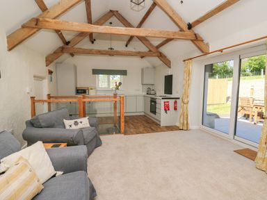 A living room with grey sofas and a kitchen with wooden beams on ceiling by sliding glass doors at The Parlour in Llangoedmor near Cardigan