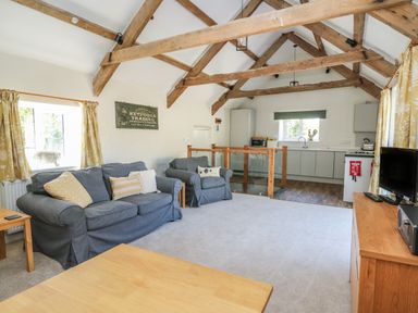 A living room with exposed wooden beams a blue sofa an armchair a wooden coffee table and a kitchen area at The Parlour in Llangoedmor near Cardigan