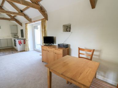 A room with wooden beams a wooden table and chair a cabinet with a television and radio and a kitchen area at The Parlour in Llangoedmor near Cardigan