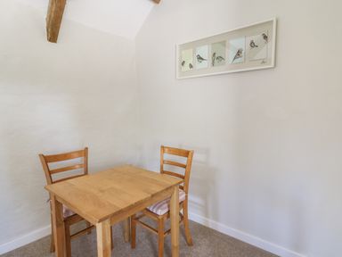 A small wooden table with two wooden chairs and a framed bird illustration on the wall at The Parlour in Llangoedmor near Cardigan