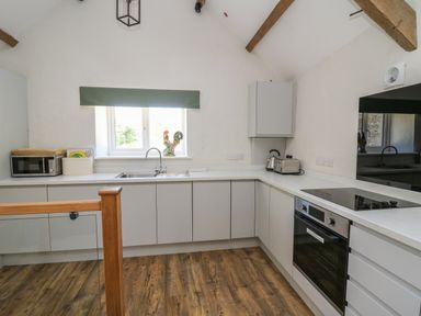 A kitchen with white cabinets wood flooring a sink under a window microwave oven toaster kettle and stove at The Parlour in Llangoedmor near Cardigan