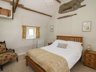 A bedroom with a wooden bed and bedside tables next to a small window with yellow curtains at The Parlour in Llangoedmor near Cardigan