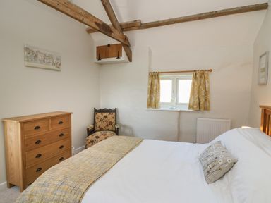 A bedroom with a bed chest of drawers armchair and small window with curtains at The Parlour in Llangoedmor near Cardigan