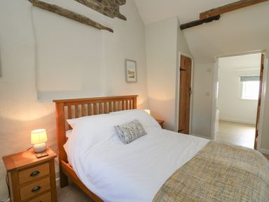 A bedroom with a wooden bed frame bedside tables with lamps and a door leading to another room at The Parlour in Llangoedmor near Cardigan