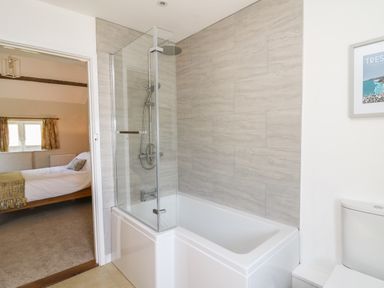 A bathroom with a bathtub shower combination and a toilet next to a bedroom at The Parlour in Llangoedmor near Cardigan