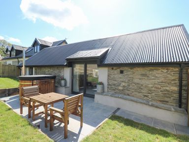 An outdoor patio with wooden table and chairs a hot tub and stone wall at The Parlour in Llangoedmor near Cardigan