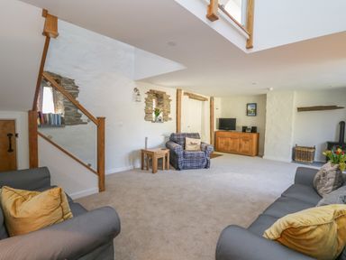 A living room with sofas pillows a plaid armchair a wooden cabinet with a tv a fireplace and flowers on a table at Cattle Tree Cottage in Llangoedmor near Cardigan