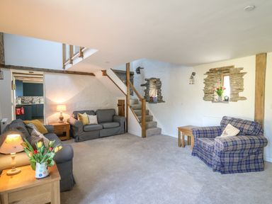 A living room with sofas a wooden side table stairs and exposed stone wall at Cattle Tree Cottage in Llangoedmor near Cardigan