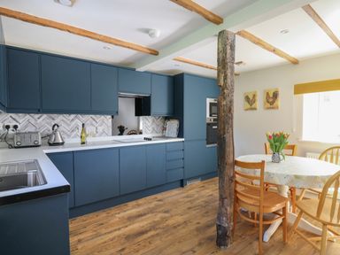 A kitchen with blue cabinets a white countertop a round dining table with wooden chairs and a vase of flowers at Cattle Tree Cottage Llangoedmor near Cardigan