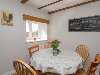 A dining room with a round table covered with a patterned tablecloth and wooden chairs at Cattle Tree Cottage in Llangoedmor near Cardigan
