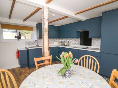 A kitchen with blue cabinets wooden chairs and a table with flowers at Cattle Tree Cottage in Llangoedmor near Cardigan