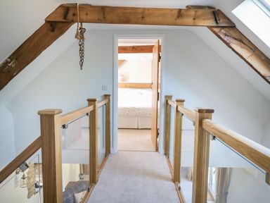 A hallway with wooden and glass railings leading to a bedroom with a bed visible through an open door at Cattle Tree Cottage in Llangoedmor near Cardigan