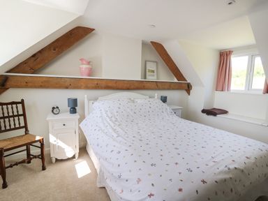 A bedroom with a double bed floral bedding wooden chair bedside tables and exposed wooden beams at Cattle Tree Cottage Llangoedmor near Cardigan