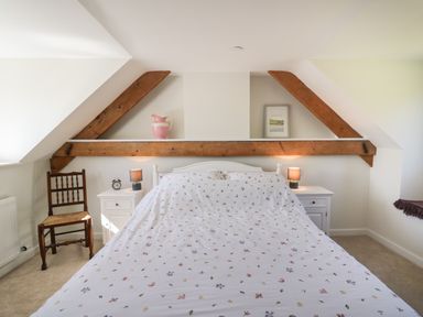 A bedroom with a bed covered in floral bedding two nightstands with lamps a wooden chair and exposed wooden beams at Cattle Tree Cottage Llangoedmor near Cardigan